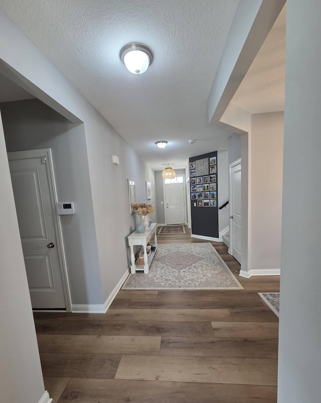 hallway with a textured ceiling, stairs, baseboards, and wood finished floors