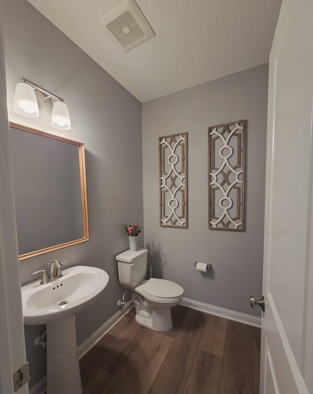half bath featuring toilet, baseboards, visible vents, and wood finished floors