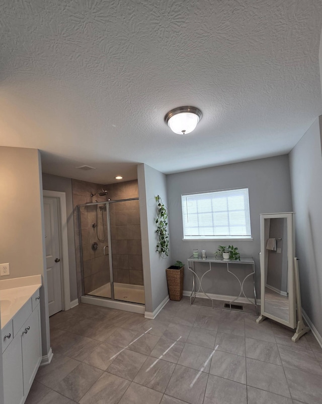 full bath featuring vanity, a textured ceiling, visible vents, a stall shower, and baseboards