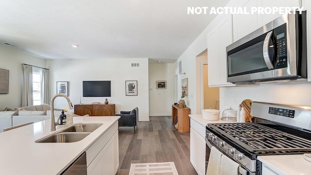 kitchen with a sink, stainless steel appliances, white cabinetry, open floor plan, and light countertops