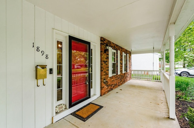 doorway to property featuring covered porch and brick siding