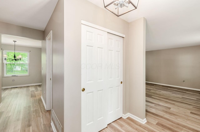hallway with an inviting chandelier, light wood-style flooring, and baseboards