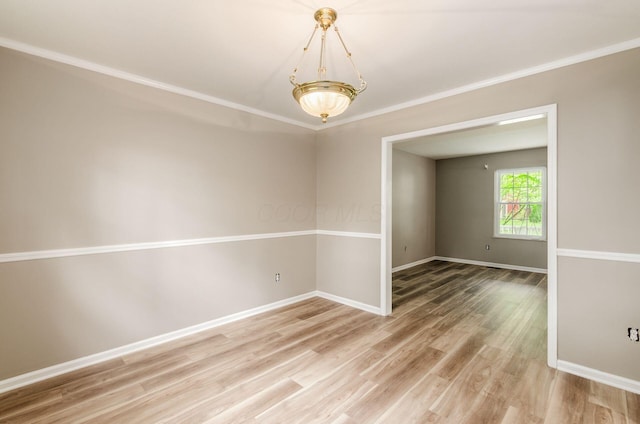 spare room featuring light wood finished floors, crown molding, and baseboards