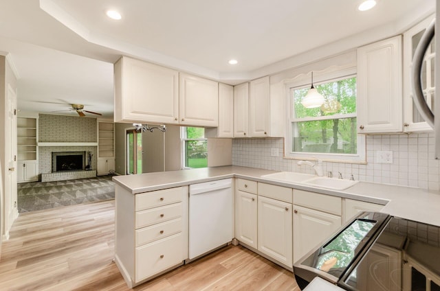 kitchen with a sink, a peninsula, dishwasher, ceiling fan, and light wood-style flooring