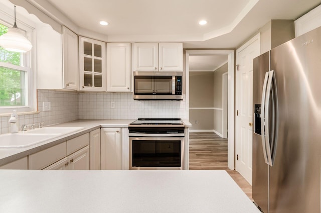 kitchen with a sink, stainless steel appliances, white cabinets, light countertops, and tasteful backsplash
