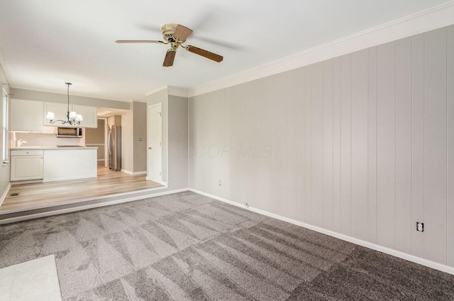 unfurnished living room with light colored carpet, baseboards, ceiling fan with notable chandelier, and ornamental molding