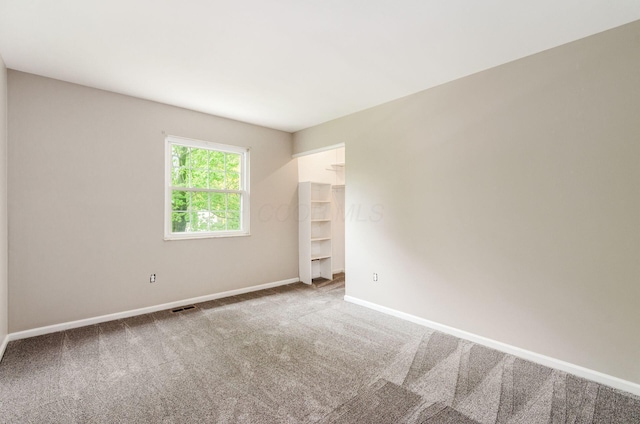 unfurnished room with carpet, visible vents, and baseboards