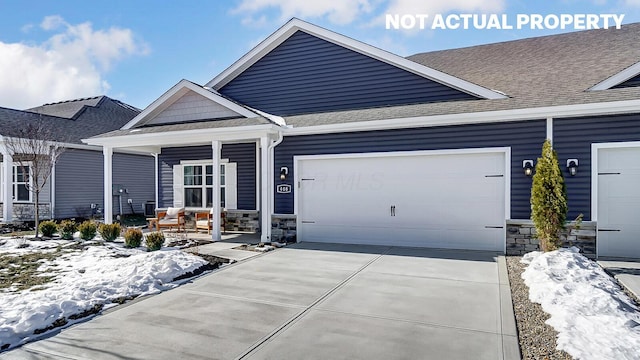 craftsman-style home featuring a shingled roof, a porch, driveway, and stone siding