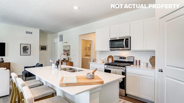 kitchen featuring a sink, independent washer and dryer, a kitchen breakfast bar, an island with sink, and appliances with stainless steel finishes