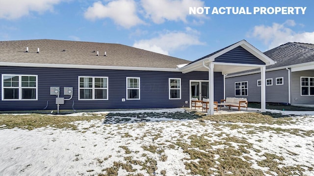 snow covered back of property with an outdoor hangout area, a shingled roof, and a patio area