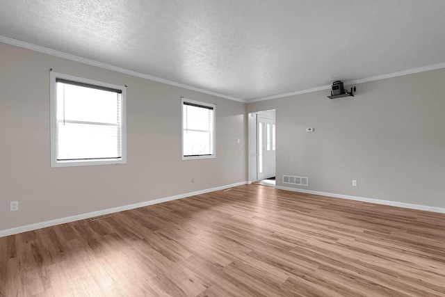 spare room featuring ornamental molding, light wood-style flooring, a textured ceiling, and visible vents
