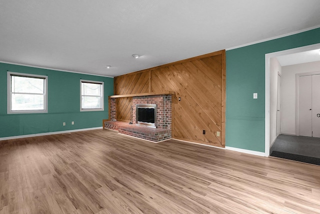 unfurnished living room featuring wood walls, wood finished floors, a fireplace, crown molding, and baseboards