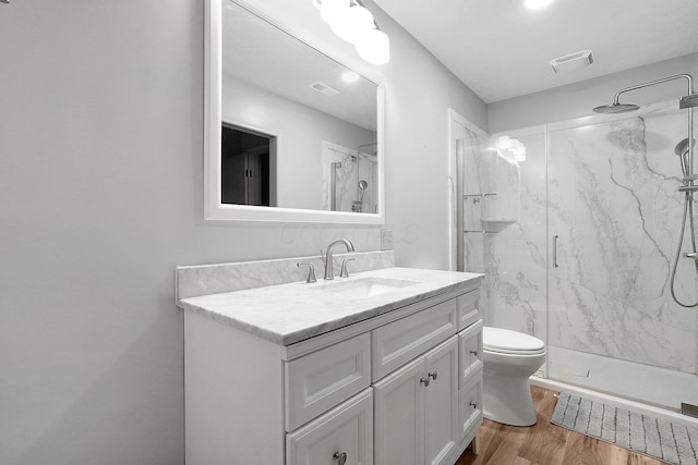 bathroom featuring toilet, wood finished floors, vanity, a marble finish shower, and visible vents