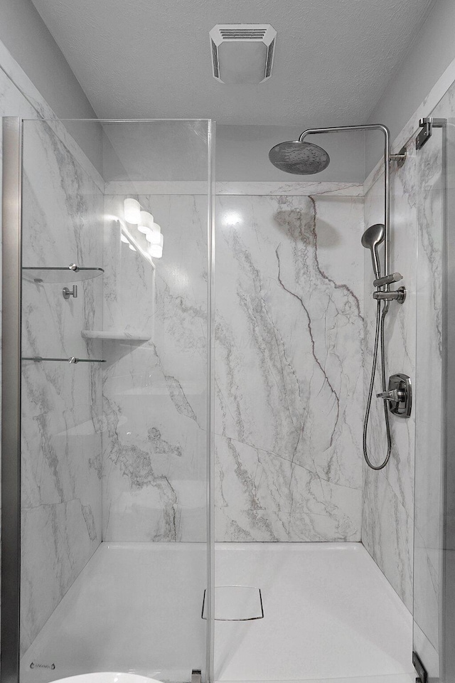 full bath featuring a marble finish shower, visible vents, and a textured ceiling