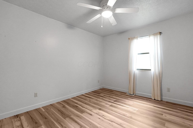 spare room featuring light wood finished floors, a textured ceiling, baseboards, and a ceiling fan