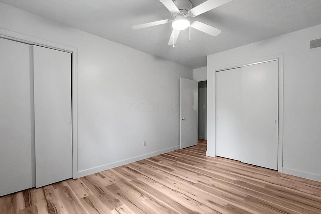 unfurnished bedroom featuring baseboards, light wood finished floors, multiple closets, and a ceiling fan