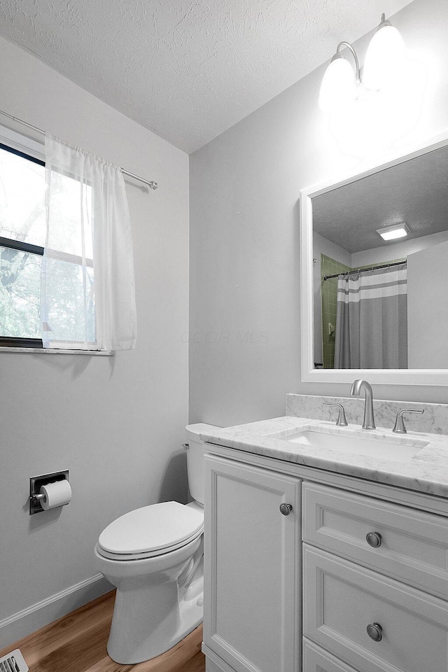 full bathroom with toilet, wood finished floors, a textured ceiling, baseboards, and vanity