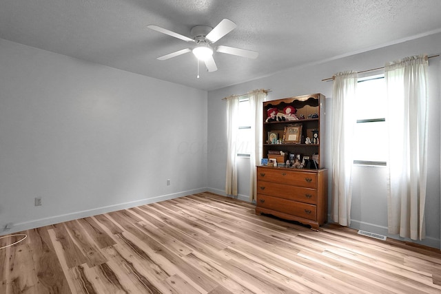 spare room with ceiling fan, visible vents, light wood-type flooring, and a textured ceiling