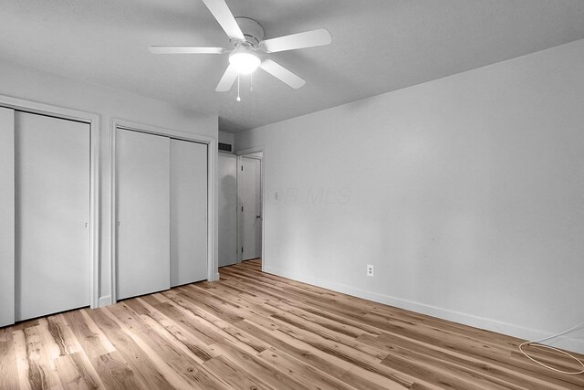 unfurnished bedroom with a ceiling fan, baseboards, visible vents, light wood-style floors, and multiple closets