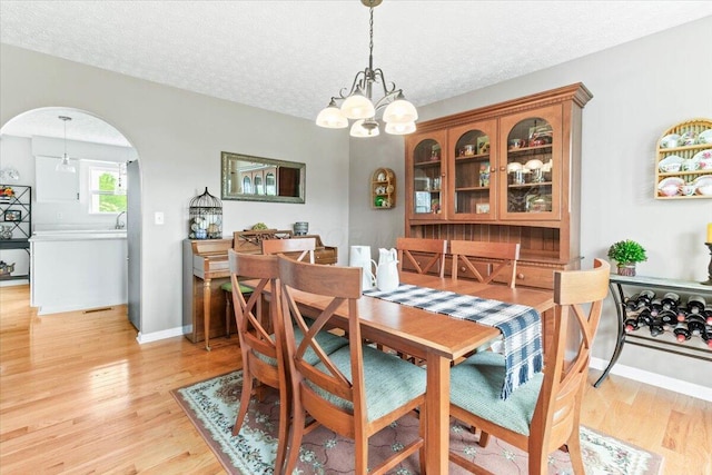 830 Avalon Dr, Pickerington, OH 43147 - dining area featuring a chandelier, light wood finished floors, arched walkways, a textured ceiling, and baseboards