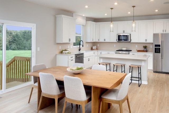 kitchen featuring stainless steel appliances, light wood-type flooring, a healthy amount of sunlight, decorative backsplash, and a kitchen island