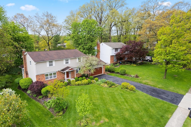 view of front of home featuring a chimney, driveway, brick siding, a garage, and a front yard
