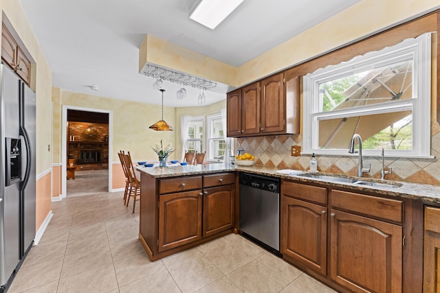kitchen with light stone counters, a sink, a peninsula, backsplash, and stainless steel appliances