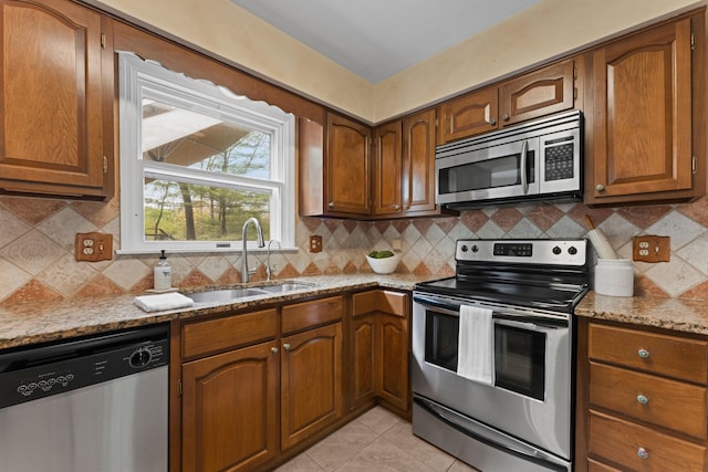 kitchen with a sink, brown cabinetry, stainless steel appliances, decorative backsplash, and light stone countertops