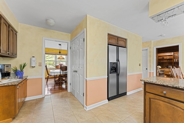 kitchen with light tile patterned floors, baseboards, light stone counters, stainless steel fridge, and brown cabinets