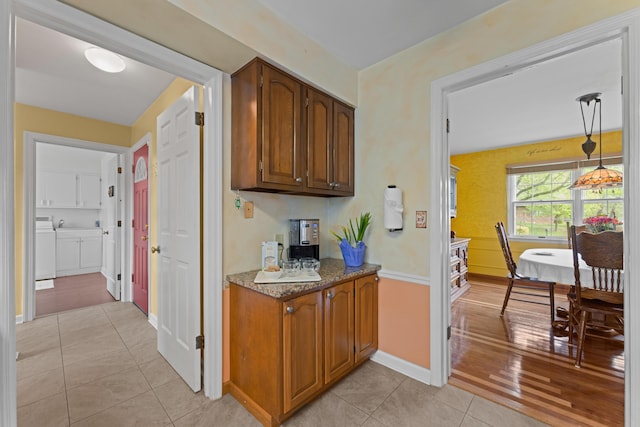 interior space with pendant lighting, baseboards, light tile patterned flooring, washer and clothes dryer, and brown cabinets