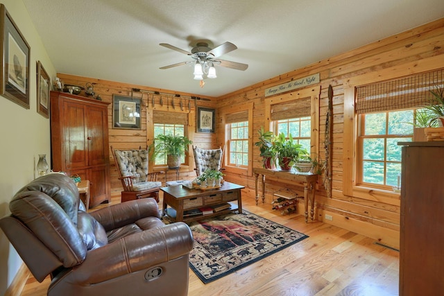 living room with a ceiling fan, wood walls, and light wood-style flooring