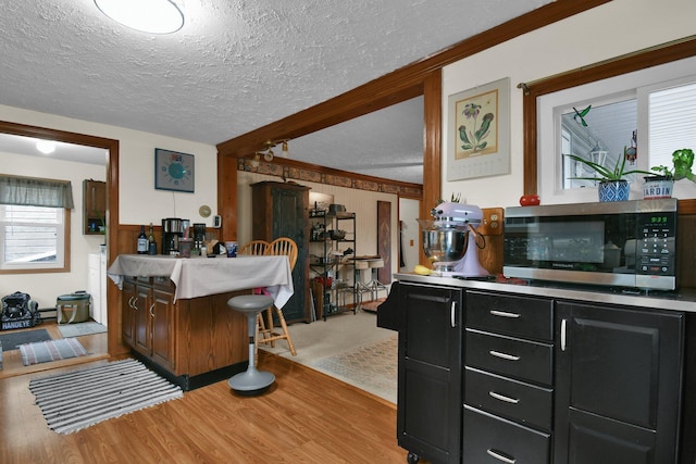 kitchen with stainless steel microwave, a textured ceiling, dark cabinetry, and beamed ceiling