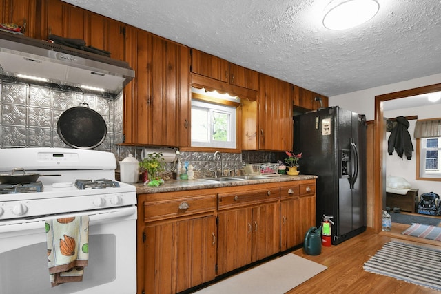 kitchen featuring brown cabinetry, range hood, a sink, black fridge, and gas range gas stove