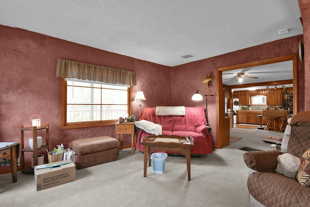 carpeted living area with ceiling fan, a textured ceiling, a textured wall, and visible vents