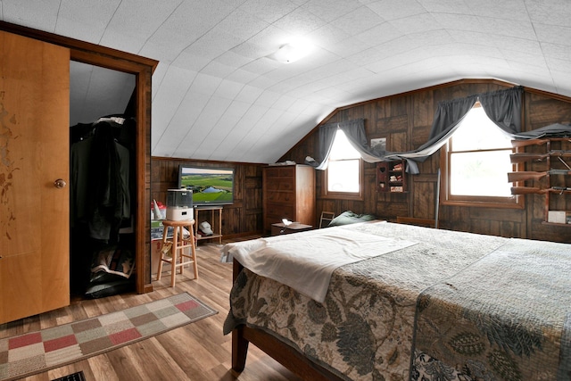 bedroom with vaulted ceiling, wooden walls, and wood finished floors