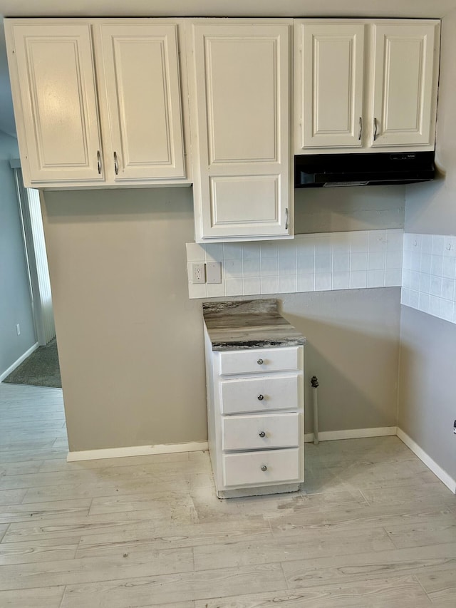 1621 Burley Dr, Columbus, OH 43207 - kitchen with under cabinet range hood, decorative backsplash, light wood-type flooring, and white cabinetry