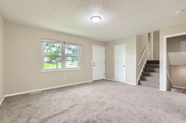 carpeted spare room with baseboards, a textured ceiling, stairway, and a smoke detector