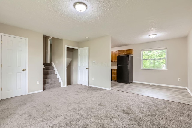 unfurnished bedroom featuring freestanding refrigerator, light colored carpet, a textured ceiling, and baseboards