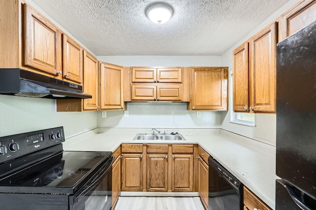 kitchen with black appliances, under cabinet range hood, a sink, a textured ceiling, and light countertops