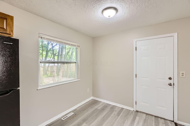 spare room with light wood finished floors, a textured ceiling, and baseboards