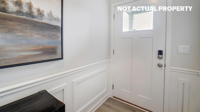 doorway to outside with wainscoting, a decorative wall, and light wood-style floors