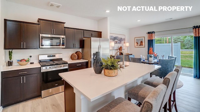 kitchen with a center island with sink, appliances with stainless steel finishes, a kitchen bar, and light wood-style floors