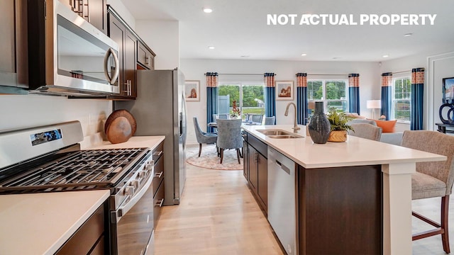 kitchen featuring light wood finished floors, a sink, stainless steel appliances, open floor plan, and light countertops
