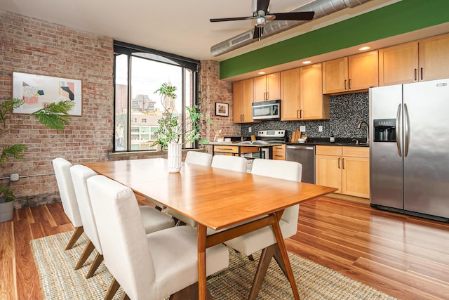 dining room with a ceiling fan, brick wall, and light wood-type flooring