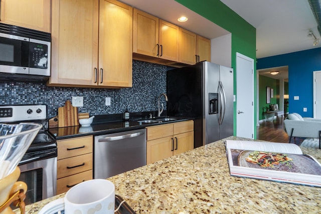 kitchen with light brown cabinets, light stone counters, a sink, backsplash, and stainless steel appliances