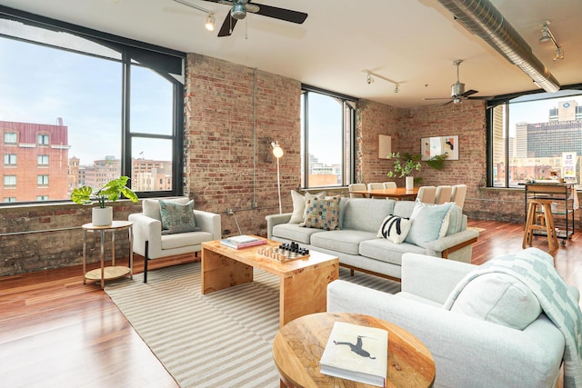 living room with track lighting, wood finished floors, ceiling fan, and brick wall