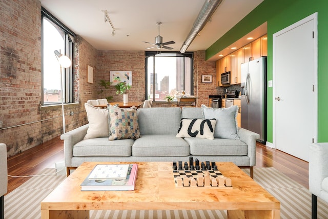 living area with brick wall, light wood-type flooring, and a ceiling fan