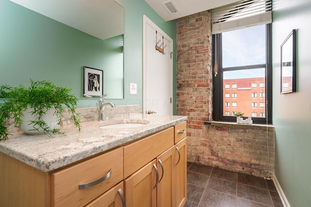bathroom with a healthy amount of sunlight, vanity, brick wall, and visible vents