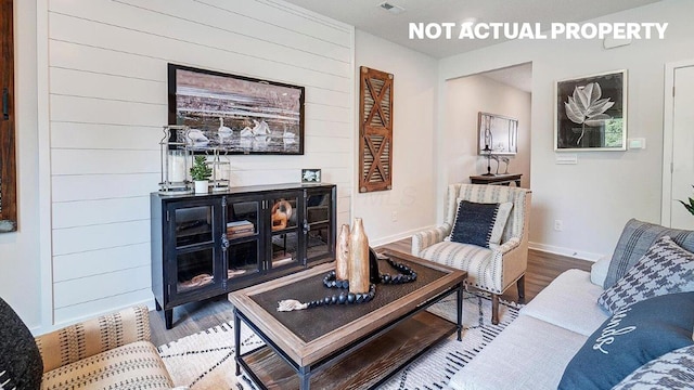 living room featuring wooden walls, baseboards, visible vents, and wood finished floors