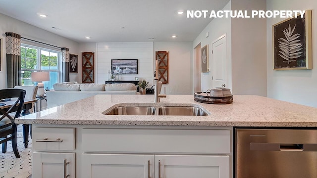 kitchen with stainless steel dishwasher, light stone counters, a sink, open floor plan, and white cabinets
